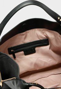 Innerhalb einer schwarzen Handtasche ist ein hellrosa Futter sichtbar, das eine kleine Reißverschlusstasche mit einem Markenetikett aufweist. Die Tasche hat goldene Akzente.