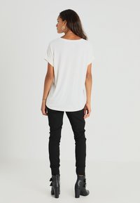 Laisvai krentantis baltas marškinėliai su apvyniotomis rankovėmis, derinami su juodomis slim-fit kelnėmis ir juodais kulkšnių batais su masyviu kulnu.