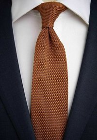 Gebreide stropdas in een rijke verbrande oranje kleur met een textuurpatroon, gedragen over een frisse witte blouse en een donkerblauwe colbert.