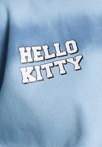 Světle modrý bavlněný svetr se výraznou bílou grafikou "HELLO KITTY" v hravém písmu. Hladká textura s gradientním efektem.