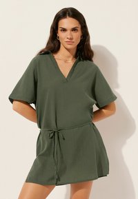 Vestido corto verde con escote en V y mangas cortas. Presenta un cinturón ajustable en la cintura y un corte relajado. Está hecho de un tejido ligero.
