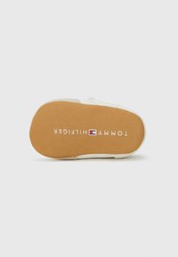 Hvit sneaker såle med en brun gummibunn, med teksten "TOMMY HILFIGER" i hvit skrift, og logoen i rød, hvit og blå.