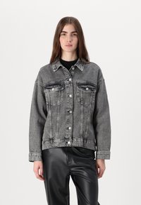 Gray denim jacket with a button-up front, two chest pockets, and a relaxed fit. Worn over a black knit top, paired with black leather pants.