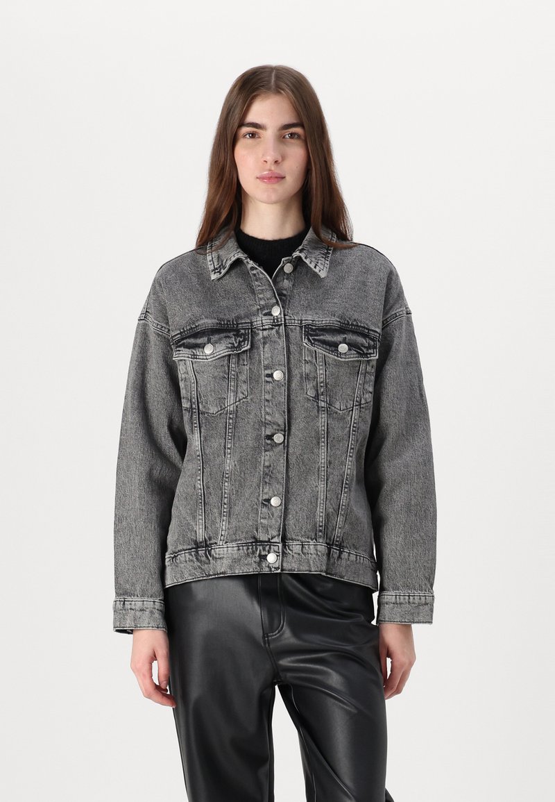 Gray denim jacket with a button-up front, two chest pockets, and a relaxed fit. Worn over a black knit top, paired with black leather pants.