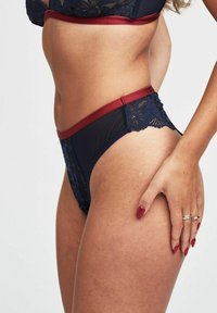 Mutande in pizzo blu navy con cintura bordeaux. Il design presenta motivi floreali e materiale semi-trasparente. Gli accenti includono bordi scallop.