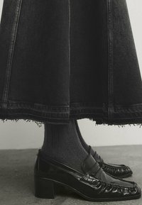 Mustap denim-hame, jossa on revitty helma, yhdistettynä kiiltäviin mustiin loafer-kenkiin ja tummiin ribbauskaihin. Korosta tekstuureja ja kontrastisia materiaaleja.