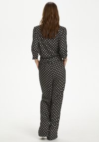 Schwarzer Jumpsuit mit tailliertem Schnitt, dreiviertellangen Ärmeln und floralem Muster. Glatte Textur mit weitem Bein und dezenten Details.