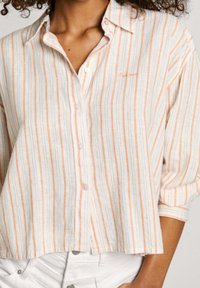Short-sleeve, collared shirt in white and peach stripes. Features a button closure and soft, textured fabric. Casual fit with a curved hem.