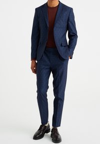 Navy patterned suit with a slim fit, featuring a textured design. Accompanied by a maroon crew neck sweater and brown lace-up shoes.