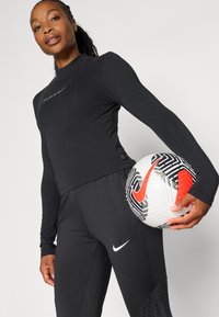 Musta pikk-pika varrukatega spordijakk, millel on "PARIS" logo, koos mustade hästi istuvate pükstega. Mudel hoiab mustrilist valget jalgpalli punaste aktsentidega.