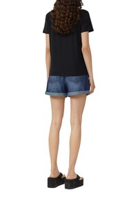 T-shirt noir à manches courtes associé à un short en denim retroussé, mettant en valeur une texture douce et un design décontracté, porté avec des sandales à plateforme noires.