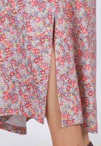 Kleid mit Blumenmuster in Helllila mit roten, grünen und lavendelfarbenen Blumen. Verfügt über einen seitlichen Schlitz und einen gekurvten Saum. Weicher Stoff.