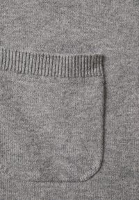 Gros plan sur un tissu gris tricoté avec une poche rectangulaire ornée d'un bord côtelé sur le bord supérieur.