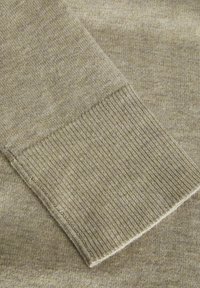 Helle beige Strickpullover mit einem gerippten Bund, der eine glatte Textur und subtile Farbvariationen aufweist. Wunderschön gearbeitete Details sind sichtbar.
