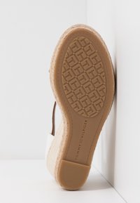 Semelle en wedge en espadrille avec un dessus en jute texturé, couleur beige, et semelle en caoutchouc arborant un logo et un motif géométrique.