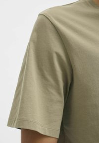 Camiseta de algodón verde oliva de mangas cortas con cuello redondo y textura suave. Costuras visibles en las mangas y el dobladillo.