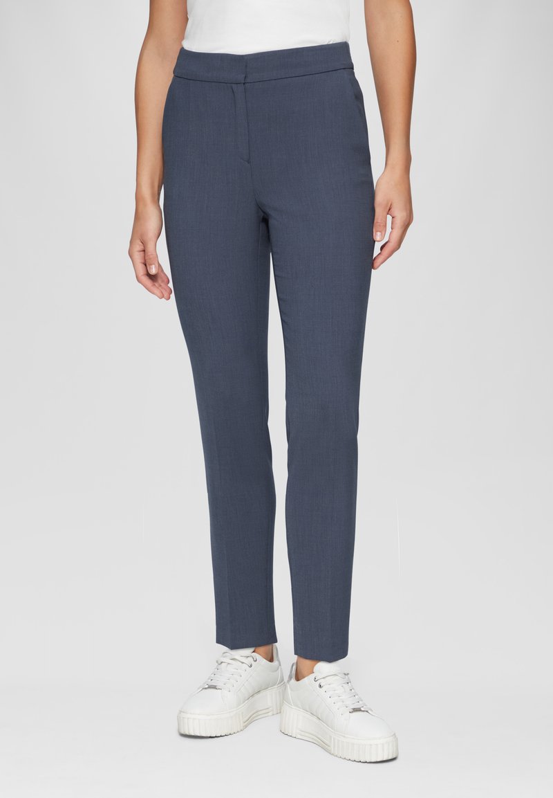 Pantalon bleu marine à coupe ajustée, jambes droites et texture lisse. Associé à des baskets blanches épaisses pour le contraste.