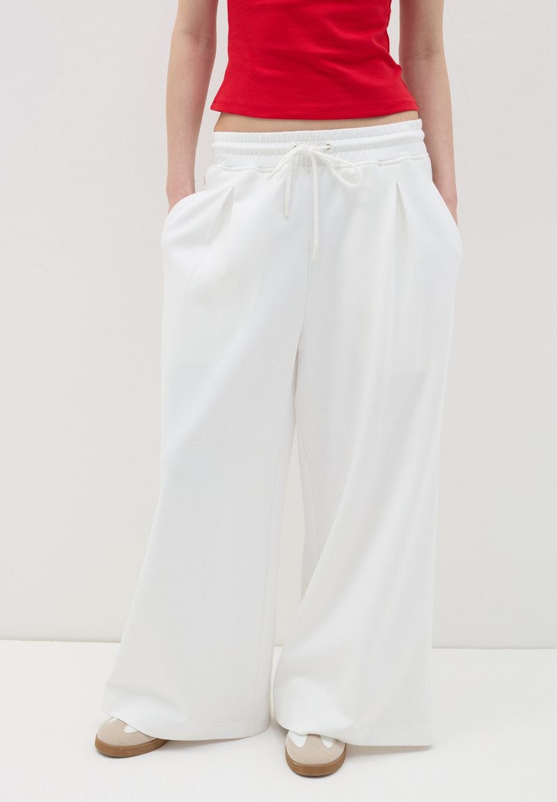 Pantalones anchos blancos con cintura ajustable, con bolsillos laterales y una tela suave y ligera. Combinados con zapatos de color claro.