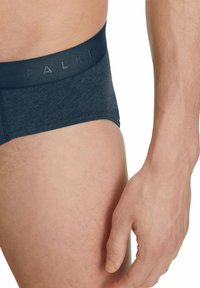 Marineblaue Baumwollslips mit glatter Textur. Der Bund trägt den eingeprägten Markennamen 'FALKE'. Nahaufnahme der Seitenansicht mit sichtbarer Haut.