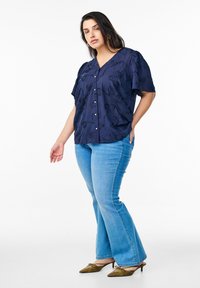 Blusa blu navy a fantasia floreale con maniche a campana corte e bottoni, abbinata a jeans svasati azzurri chiari e ballerine verdi oliva a punta.