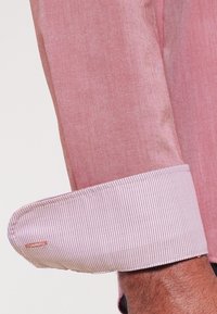 Manche de chemise rose pâle avec un poignet contrasté texturé à motif à carreaux. Tissu lisse avec un léger éclat, détail de couture simple.