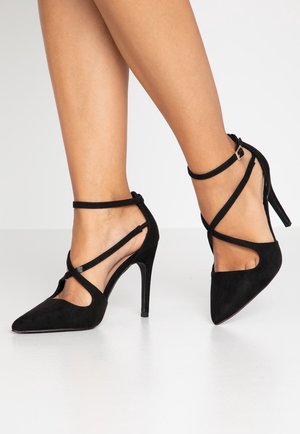 Zwarte suède high heels met spitse neuzen en gekruiste enkelbandjes, met een elegante uitstraling en een gladde textuur.