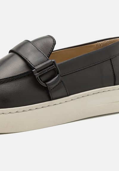 Svarta läderloafers med ett rem och spänne, med en kontrasterande beige gummisula och slät yta.