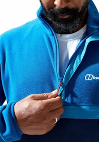 Blauwe fleece pullover met een hoge kraag, ritssluiting aan de voorkant met een contrasterende turquoise voering en een rode ritstrekt, gladde textuur, geen patronen.