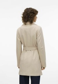 Beige plášť s páskem, má přizpůsobený límec a dlouhé rukávy, vyrobený z měkké tkaniny. Design zahrnuje mírně rozšířený lem a detail švu na zadním díle.
