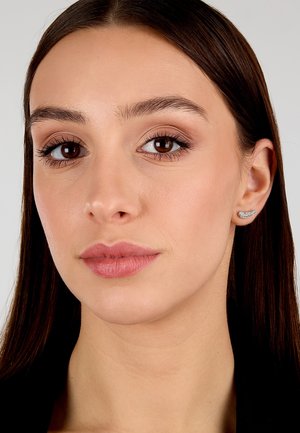 Orecchino a perno in argento con un design curvo, adornato con piccole gemme trasparenti, posizionato su uno sfondo neutro e indossato da un modello.