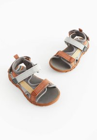 Grå og orange sandaler lavet af syntetisk materiale. Har justerbare velcro-remme og robuste gummisåler med mønstrede indersåler.