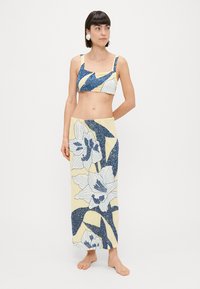 Divdaļīgs tērps, kas sastāv no īsa topa un garas svārkas. Audums ir dzeltenā krāsā ar ziliem ziedu rakstiem un spīdīgu tekstūru.