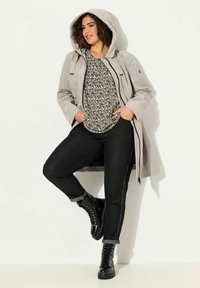 Jasnoszara kurtka wodoodporna z kapturem, czarna koszula w wzory, ciemne dżinsy z podwiniętymi mankietami i czarne buty na sznurówki. Prosty design i tekstury.