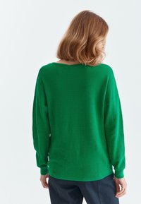 Pull en tricot côtelé vert, à coupe décontractée, épaules tombantes et manches longues. Doté d'une encolure large et d'une texture douce.