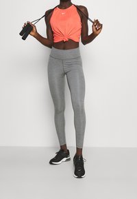 Top corto arancione con dettaglio annodato, abbinato a leggings grigi a vita alta e scarpe da ginnastica nere. Design semplice, tessuto leggero.