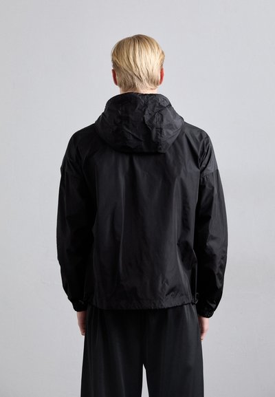 Schwarze leichte Jacke mit Kapuze, ausgestattet mit elastischen Bündchen und einem verstellbaren Saum. Glatte Textur, minimalistisches Design, keine sichtbaren Logos.