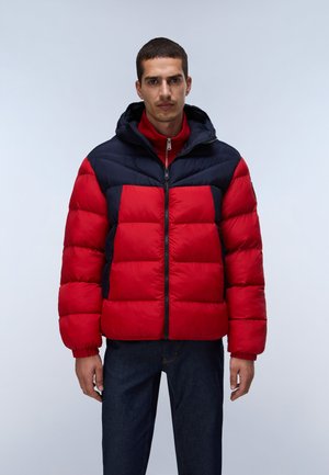 Mann trägt eine rot-schwarz farbige Steppjacke mit Kapuze und steht vor einem schlichten hellen Hintergrund.
