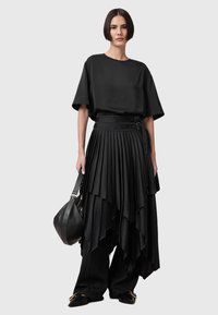 Sort outfit bestående af en løstsiddende kortærmet top og en lagdelt plisseret nederdel. Accepteret af en tekstureret sort taske og flade sko.