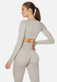 Hellgraues Langarm-Crop-Top, kombiniert mit hoch taillierten Leggings, die eine glatte Textur und ein dezentes Farbverlaufmuster aufweisen.