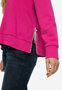 Felpa fucsia con cerniere laterali, polsini e orlo a costine. Realizzata in tessuto morbido, presenta una vestibilità rilassata e una superficie leggermente testurizzata.