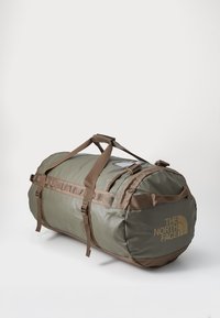 Olive green duffel bag with brown accents. Made of durable material, features carrying straps and side pocket. Logo printed on one side.