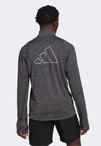 Haut de sport à manches longues, gris foncé, en tissu texturé, avec un logo Adidas blanc dans le dos et des passages pour les pouces aux poignets.