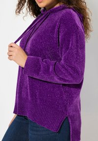 Pullover con cappuccio viola realizzato in tessuto morbido e testurizzato. Caratterizzato da polsini a coste e spacchi laterali all'orlo per una maggiore libertà di movimento.