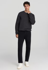 Maglione a maglia grigio scuro con scollatura a girocollo, abbinato a pantaloni neri attillati e sneakers bianche. Design semplice, tessuto texture.