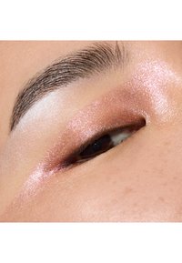 Gros plan sur un œil avec un fard à paupières rose scintillant, mettant en valeur une paupière beige chaud et un sourcil bien défini. La texture réfléchissante crée de la profondeur.