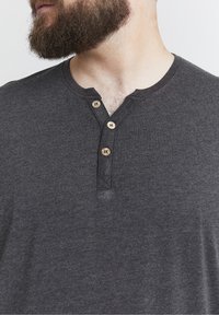 Maglietta henley grigia con maniche corte, tessuto morbido, tre bottoni in legno sul collo e un sottile design a V.
