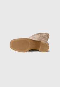 Braunes Wildleder-Stiefelette mit runder Spitze und einer strukturierten Gummisohle, die Kerben für besseren Halt sowie ein dezentes Markenlogo aufweist.