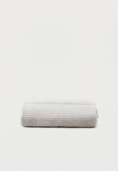 Διπλωμένη πετσέτα μπάνιου ανοιχτό γκρι με υφή περιμετρικά, τοποθετημένη σε απλό λευκό φόντο.