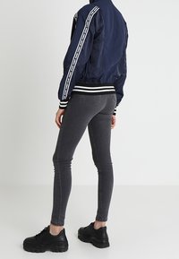 Granatowa bomberka z białymi paskami, czarne wąskie dżinsy i solidne czarne sneakersy. Elegancki design z żebrowanymi mankietami i pasem w talii.