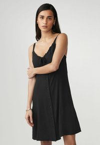 Schwarzes Kleid mit Spaghettiträgern, gerafftem Ausschnitt und einer Knopfleiste vorne. Glattes Material mit lockerer Passform.